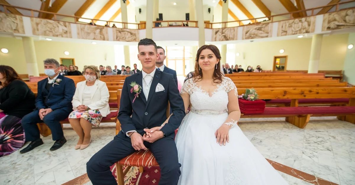 Une mariée et un marié assis dans une église magnifiquement décorée, entourés d'invités lors de leur cérémonie de mariage.