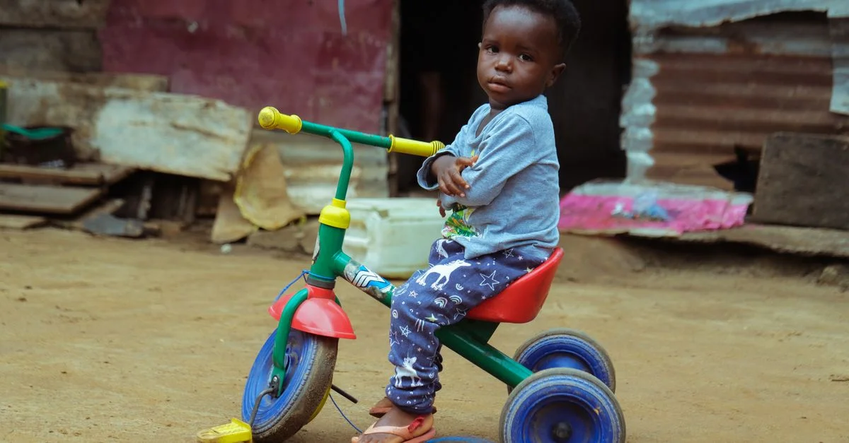 Jeune enfant sur un tricycle coloré, jouant en milieu urbain, Monrovia, Libéria.