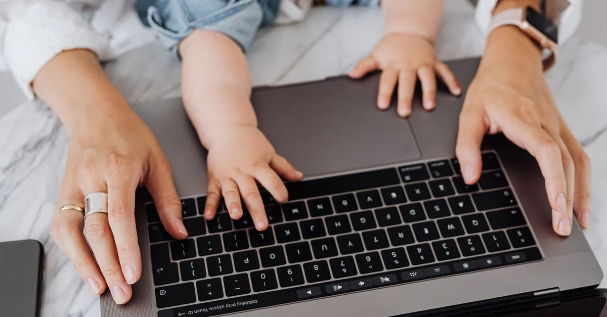 Gros plan sur les mains d'une mère et d'un enfant sur le clavier de l'ordinateur portable, symbolisant le multitâche et le lien familial.