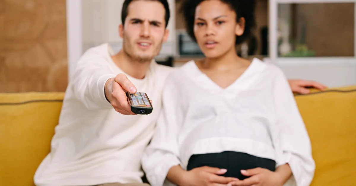Un couple assis sur un canapé, regardant la télévision ensemble avec une télécommande à la main, dans un cadre intérieur confortable.